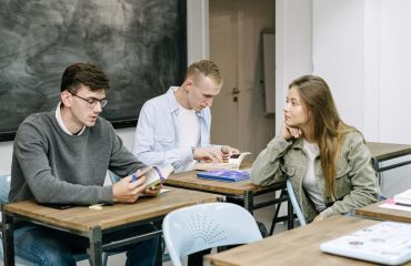 Group of young adults studying together in a classroom setting, engaged in reading and discussion.