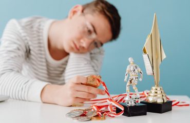 A thoughtful teenager sits by a table with various trophies and medals.